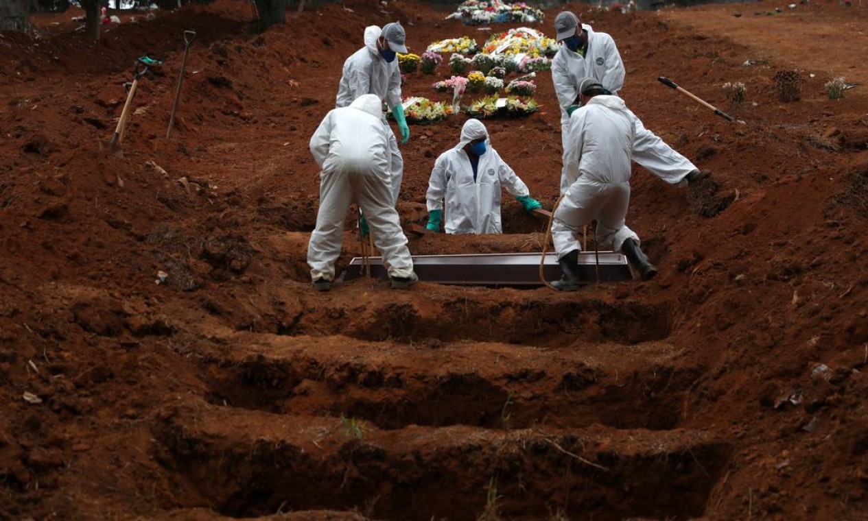 Coveiros vestindo roupas de proteção enterram o caixão de uma vítima da COVID-19, no cemitério São Luiz, em São Paulo. Até o mês de abril, o Brasil registrou mais mortes por Covid-19 do que todo o ano de 2020, quando começou a pandemia, e também ultrapassou a triste marca dos 400 mil mortos Foto: AMANDA PEROBELLI / Reuters - 04/07/2020