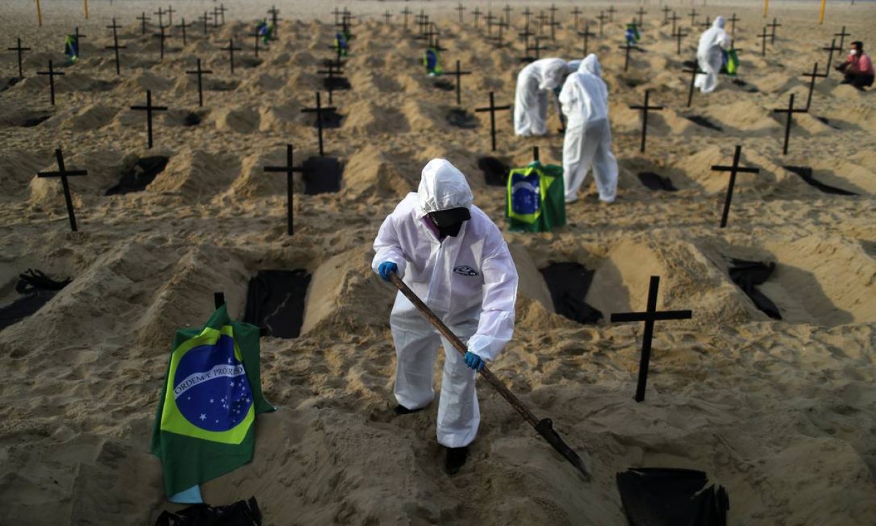 Ativistas da ONG Rio de Paz em trajes de proteção cavam sepulturas na praia de Copacabana para simbolizar os mortos pela COVID-19, durante uma manifestação no Rio de Janeiro Foto: PILAR OLIVARES / REUTERS