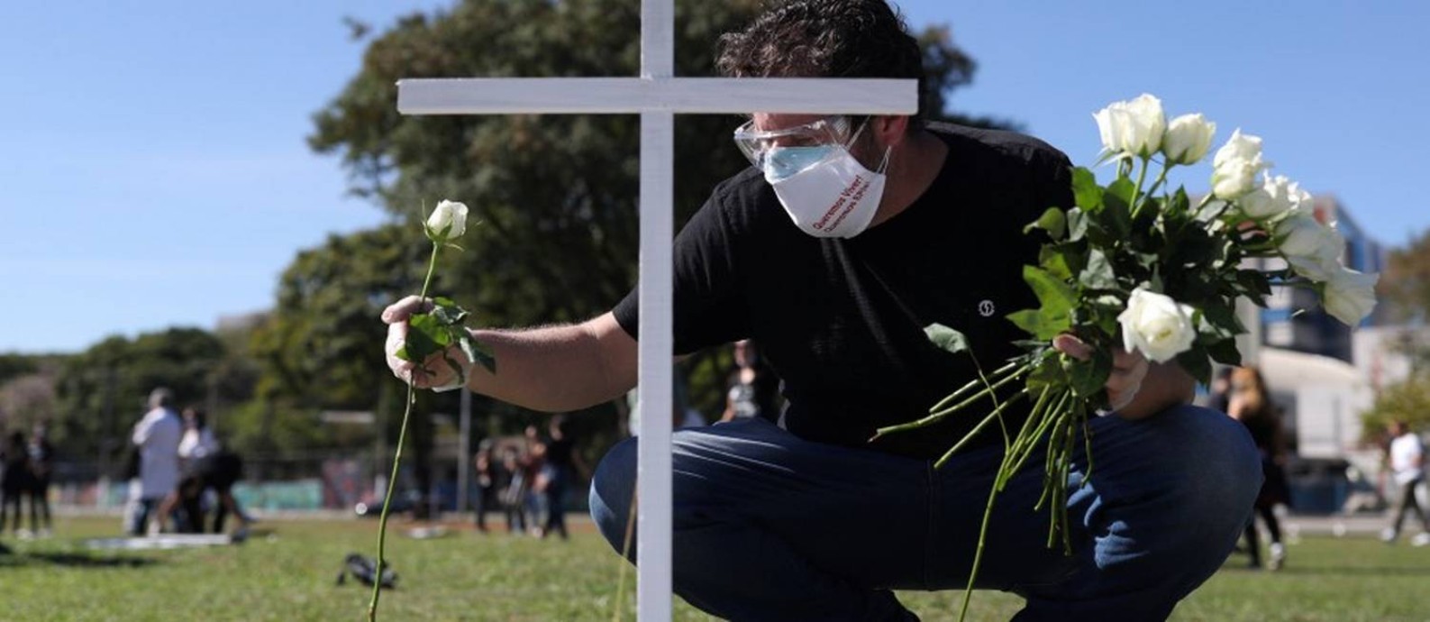 Homem coloca uma flor diante de uma cruz simbólica num protesto e homenagem a profissionais da saúde mortos pela Covid-19 em São Paulo Foto: AMANDA PEROBELLI / REUTERS