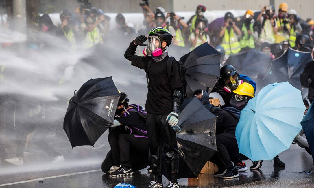 Manifestantes pró-democracia se protegem de jatos d'água da polícia durante protestos no lado de fora da sede do governo de Hong Kong Foto: ISAAC LAWRENCE / AFP
