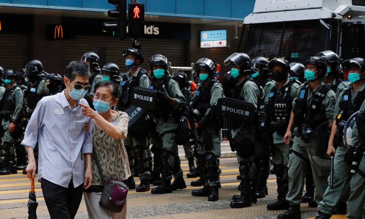 Casal passa pela polícia de enquanto manifestantes marcham durante o aniversário da devolução de Hong Kong Foto: TYRONE SIU / REUTERS
