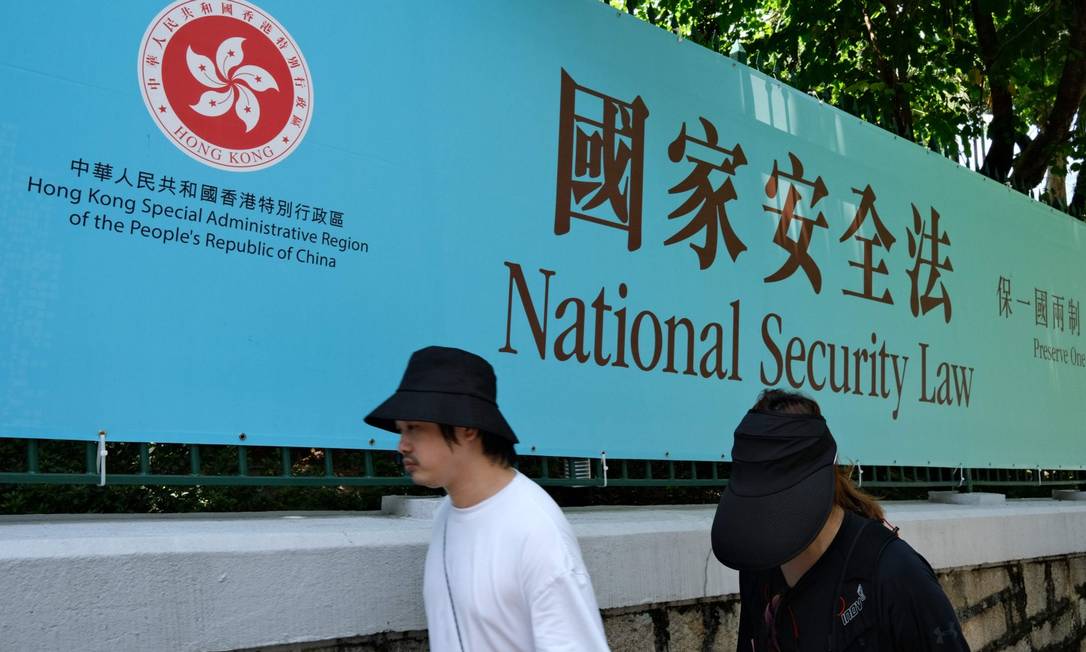 Pedestres caminham em frente a banner da lei de segurança nacional em Hong Kong Foto: ANTHONY WALLACE / AFP