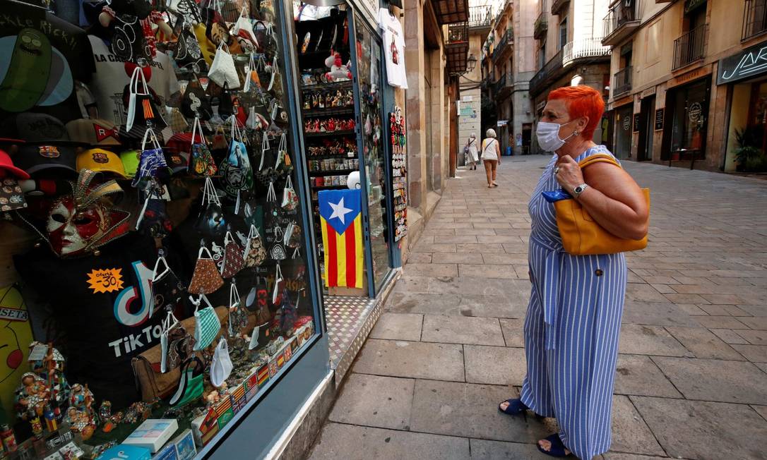 De máscara, mulher observa vitrine de loja de souvenirs em Barcelona Foto: Albert Gea / REUTERS / 27-7-2020
