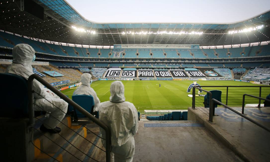Funcionários da Arena do Grêmio assistem ao jogo com roupas de proteção: futebol em tempos de Covid-19 Foto: DIEGO VARA/REUTERS