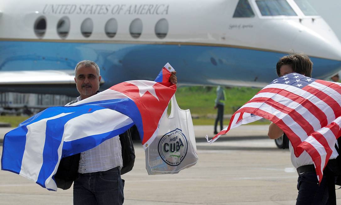 Passageiros seguram bandeiras de Cuba e dos EUA após pousarem do primeiro voo comercial entre os dois países, em 2016 Foto: YAMIL LAGE / AFP