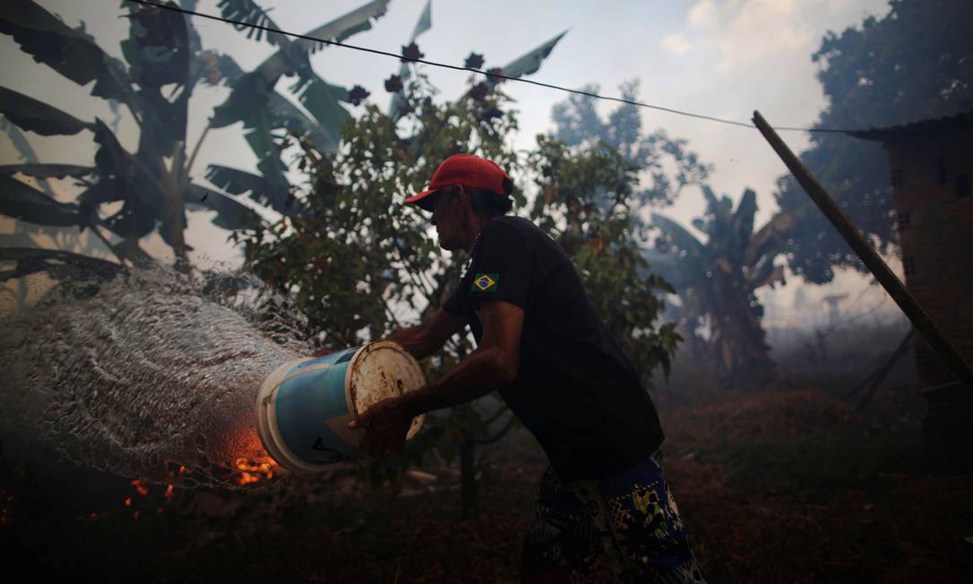 Rosalino de Oliveira joga água tentando proteger sua casa enquanto o fogo se aproxima em uma área da floresta amazônica, perto de Porto Velho, Rondônia Foto: UESLEI MARCELINO / REUTERS