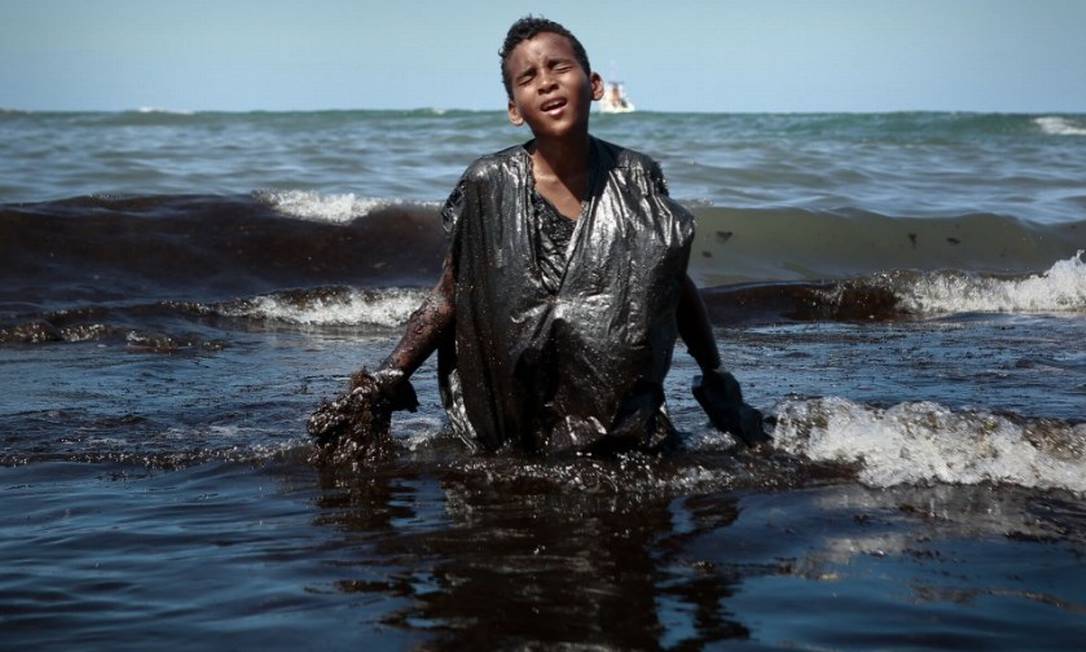 Menino deixa água da praia onde trabalhava na remoção de óleo, em Cabo de Santo Agostinho (PE): voluntários criticaram falta de equipamentos de proteção individual Foto: Leo Malafaia/AFP/21-10-2019