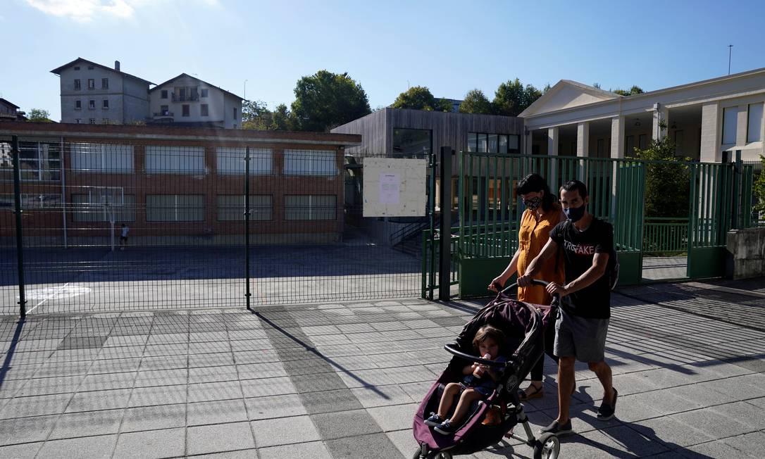Casal caminha com criança em carrinho em frente a uma escola fechada no País Basco, na Espanha, na última quinta-feira (10); instituições foram fechadas na região depois que diversos professores testaram positivo para a Covid-19 Foto: VINCENT WEST / REUTERS