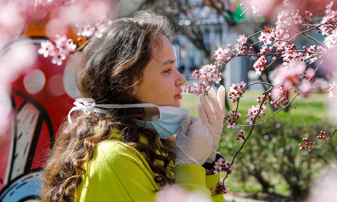Jovem tira a máscara de proteção contra o novo coronavírus para sentir cheiro das flores em uma árvore Foto: OGNEN TEOFILOVSKI / Reuters