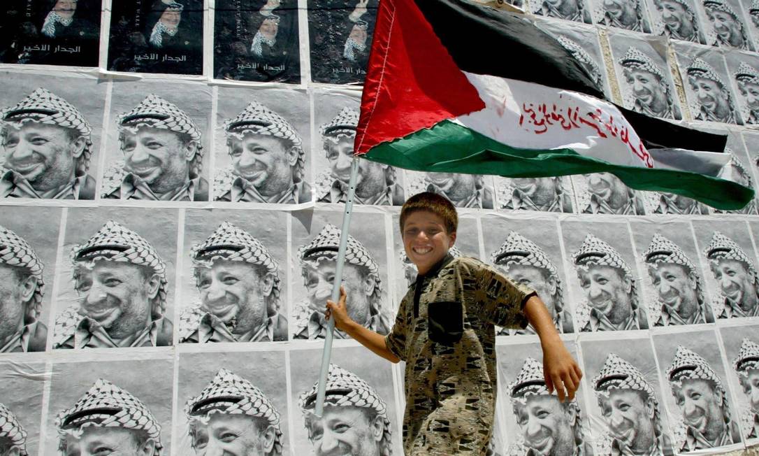 Em Gaza, menino carrega bandeira da Palestina em frente a cartazes com o rosto de Yasser Arafat Foto: Fayez Nureldine / AFP / 5-6-2013
