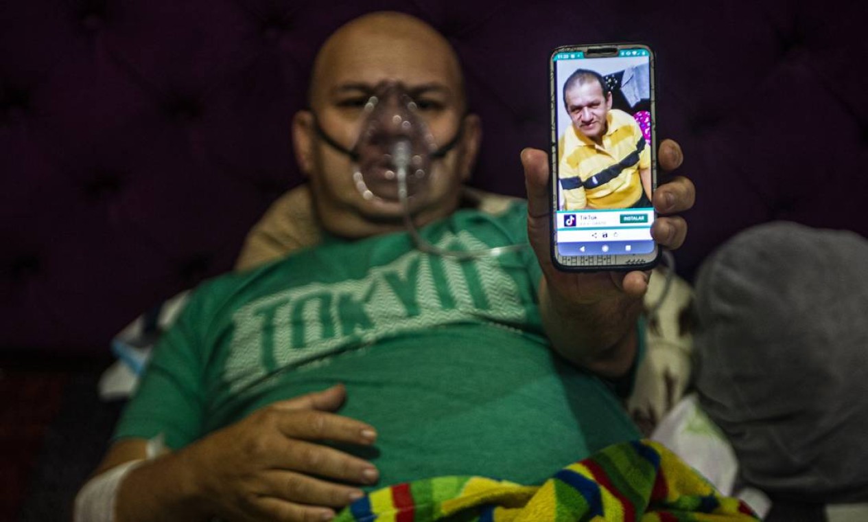O venezuelano Wilmer Hernandez, 44, mostra uma foto de seu pai, Wilmer Arcadio Hernandez, 63, enquanto ele permanece conectado a um tanque de oxigênio em sua casa, em Villa Maria del Triunfo, ao sul de Lima Foto: ERNESTO BENAVIDES / AFP