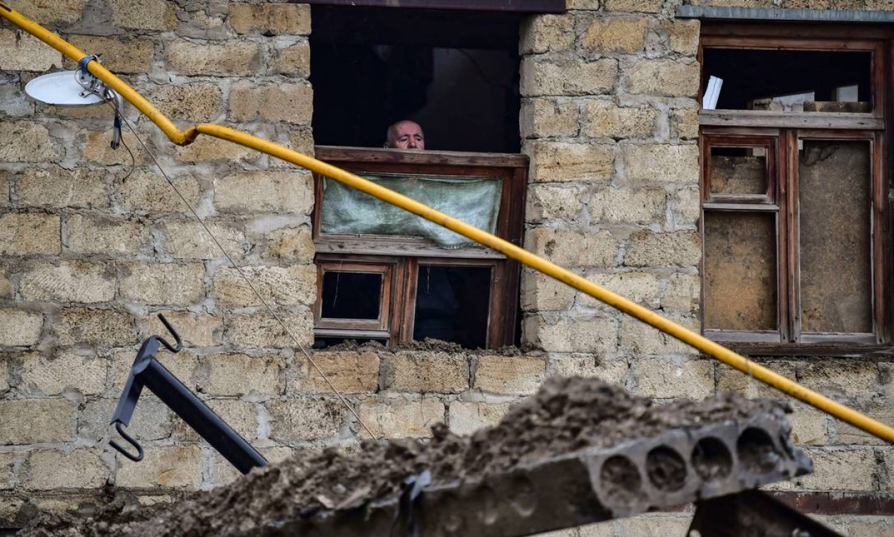 Idoso olha para fora de uma janela danificada por uma explosão na principal cidade da região separatista de Nagorno-Karabakh, Stepanakert Foto: ARIS MESSINIS / AFP