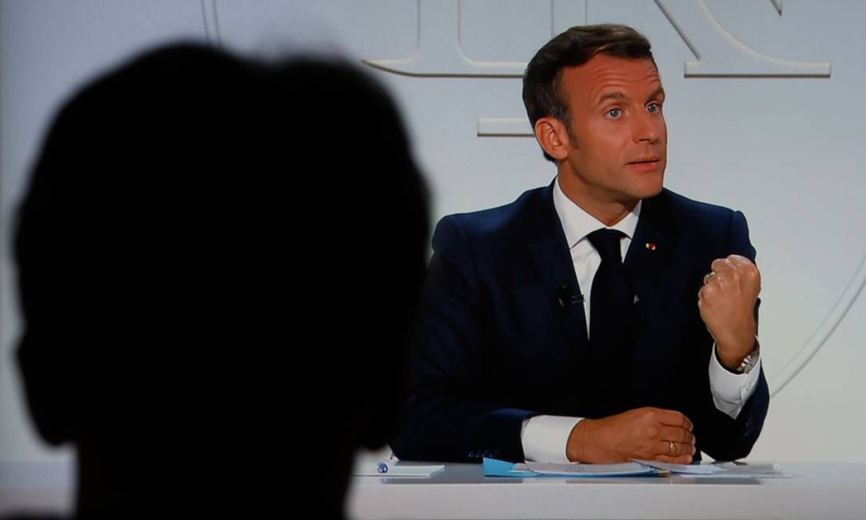 Um homem assiste a um entrevista com o presidente francês, Emmanuel Macron, que anunciou nesta quarta-feira (14) ordenou um toque de recolher noturno para Paris e oito outras cidades francesas para conter a disseminação crescente de Covid-19 no país Foto: LUDOVIC MARIN / AFP
