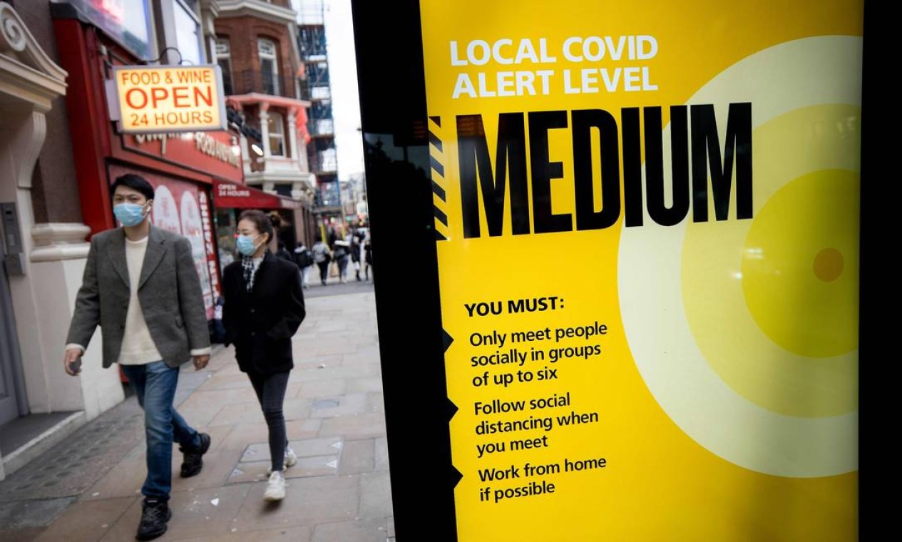 Pedestres passam por uma placa do NHS exibindo diretrizes durante a nova onda da pandemia de coronavírus, em Londres. No Reino Unido, o número de casos da Covid-19 disparou Foto: TOLGA AKMEN / AFP