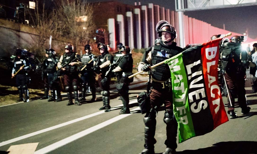 Um policial de Minnesota segura uma bandeira do caso Black Lives apreendida de um manifestante na Interestadual 94, onde manifestantes foram presos por bloquear a estrada durante uma marcha contra o racismo e o sistema político em Minneapolis, Minnesota Foto: KEREM YUCEL / AFP