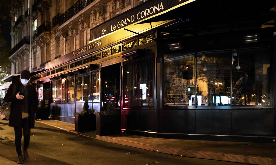 Homem caminha de máscara em frente a um café fechado em Paris, na França Foto: Joel Saget / AFP