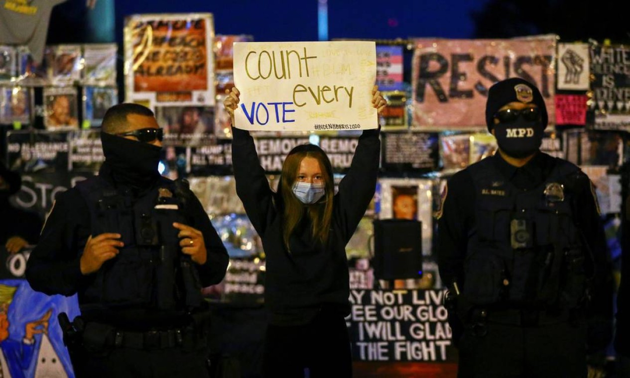 Manifestante segura uma placa entre policiais no Black Lives Matter Plaza, próximo à Casa Branca, na noite desta quinta-feira Foto: HANNAH MCKAY / REUTERS