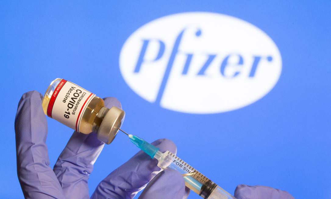 Mulher segura frasco com um adesivo "Vacina Coronavírus Covid-19" em frente ao logotipo da Pfizer Foto: Dado Ruvic / Reuters