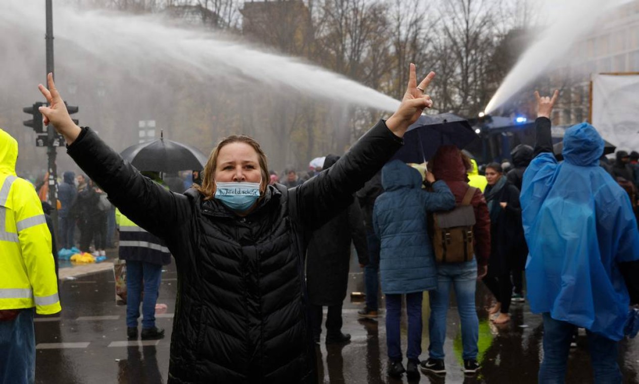Mulher faz sinal da vitória enquanto, ao fundo, polícia dispara jato de canhão d'água em manifestação contra medidas restritivas Foto: ODD ANDERSEN / AFP