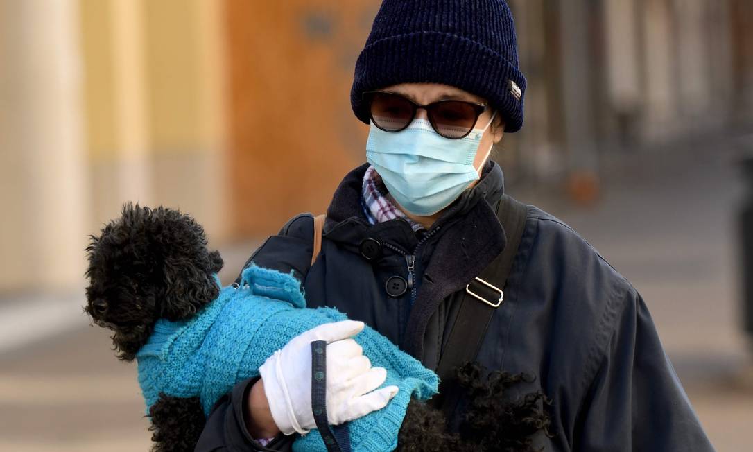 Mulher usando uma máscara protetora e luvas segura um cachorro enquanto caminha na Croácia, em meio à pandemia da Covid-19 Foto: DENIS LOVROVIC / AFP