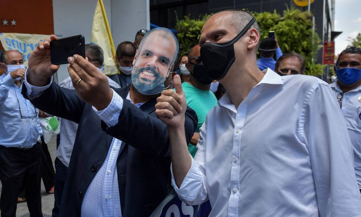 Bruno Covas (PSDB) faz selfie com homem de terno que usa máscara com a imagem do candidato à reeleição Foto: NELSON ALMEIDA / AFP - 25/11/2020