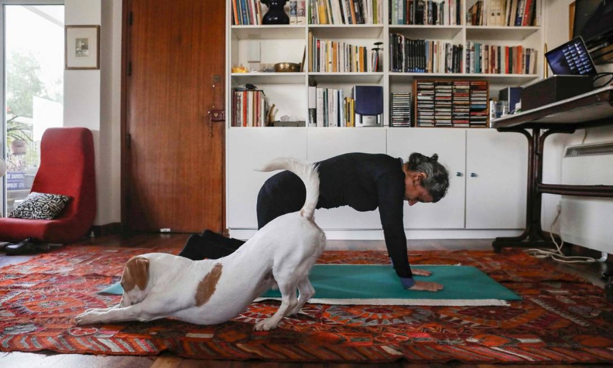 Mulher participa de uma aula de pilates online em casa, enquanto seu cachorro Elvis se estica ao lado dela, em Nicósia, enquanto restrições ao movimento e distanciamento social foram impostas em Chipre para conter a propagação do novo coronavírus Foto: CHRISTINA ASSI / AFP - 23/03/2020