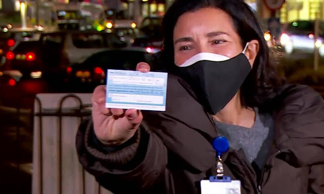 Lúcia mostra cartão de vacinação que recebeu após tomar a primeira dose da vacina contra a Covid-19 no Reino Unido. Foto: Reprodução/Globo News