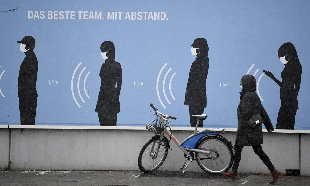 Mulher caminha em Munique, na Alemanha, em frente a um pôster "O melhor time. Com distância" Foto: Andreas Gebert / Reuters