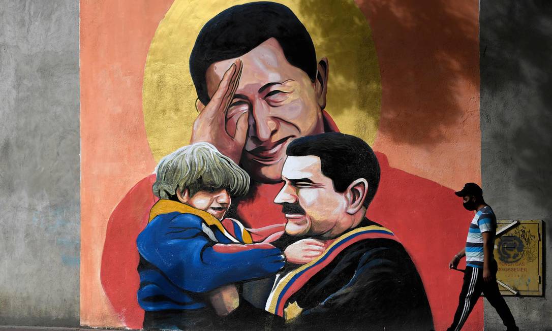 Homem passa por mural com imagens de Hugo Chávez e Nicolás Maduro em Caracas Foto: FEDERICO PARRA / AFP