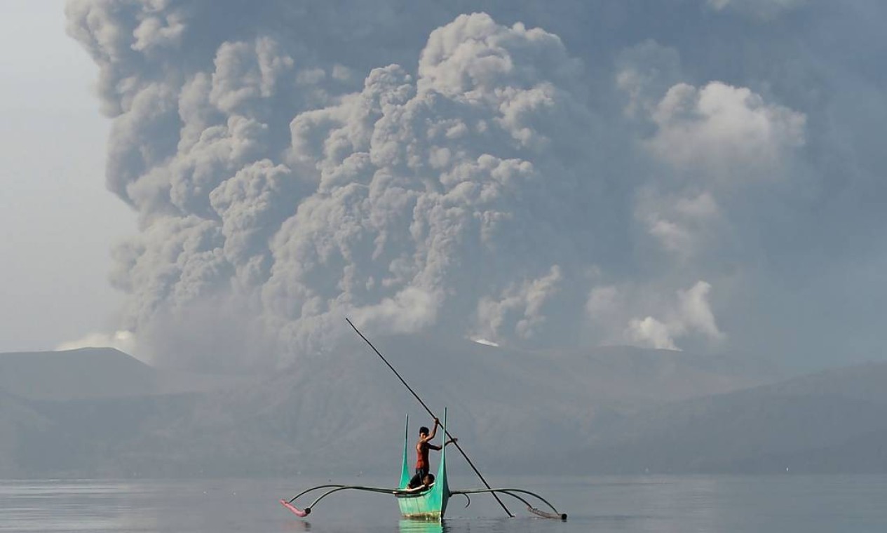 Janeiro - Jovem que mora ao pé do vulcão Taal rema enquanto o vulcão expele cinzas, na cidade de Tanauan, na província de Batangas, ao sul de Manila, Filipinas Foto: TED ALJIBE / AFP - 13/01/2020