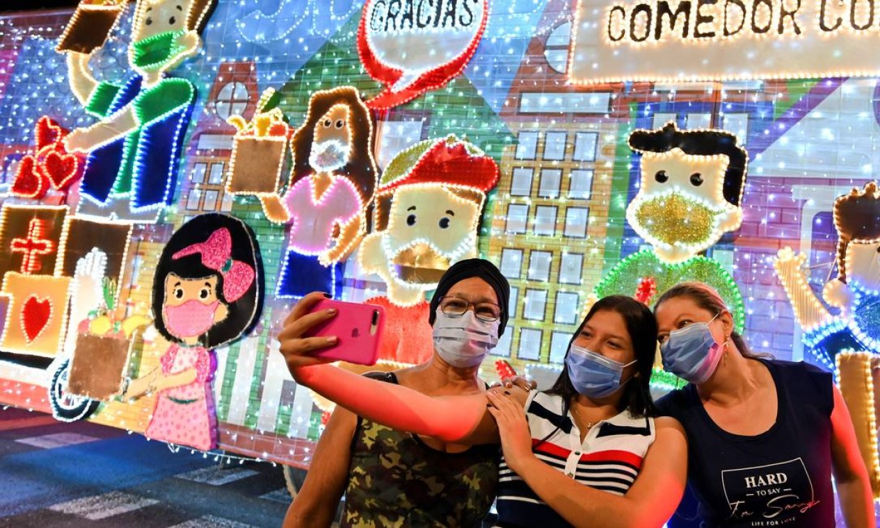 Pessoas usando máscaras fazem selfie em frente a um caminhão decorado com luzes de Natal nas ruas de Cali, Colômbia. Para evitar aglomerações, a decoração de natal este ano será itinerante, com caminhões decorados que percorrem a cidade Foto: LUIS ROBAYO / AFP