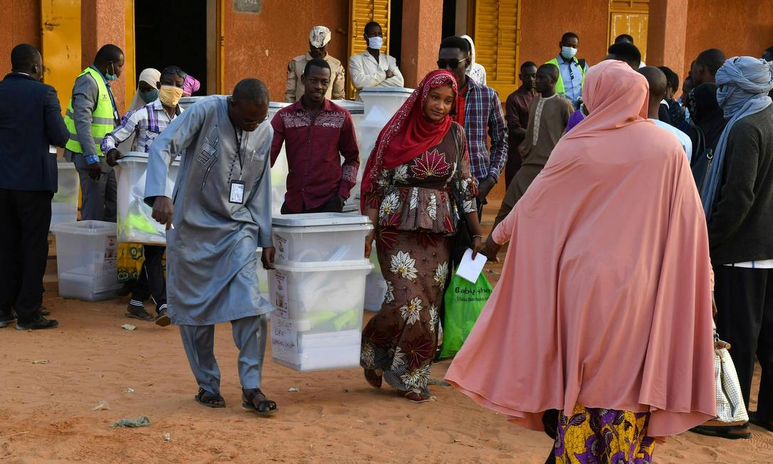 Funcionários da comissão eleitoral carregam urnas do lado de fora de uma assembleia de voto em Niamei, durante as eleições presidenciais e legislativas do Níger Foto: SOULEYMANE AG ANARA / AFP