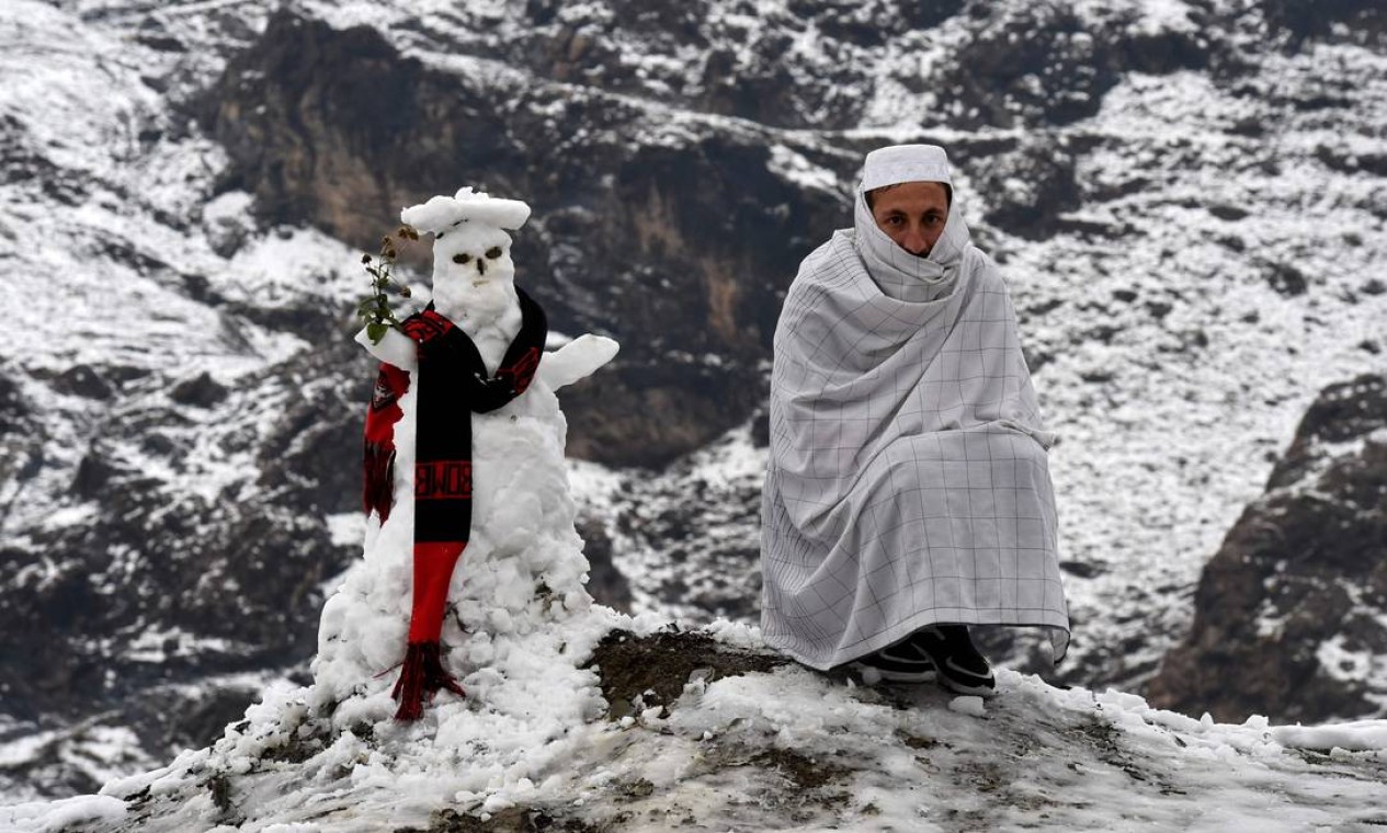 Um homem se senta ao lado de um boneco de neve após as primeiras nevascas em Landi Kotal, no Paquistão Foto: ABDUL MAJEED / AFP