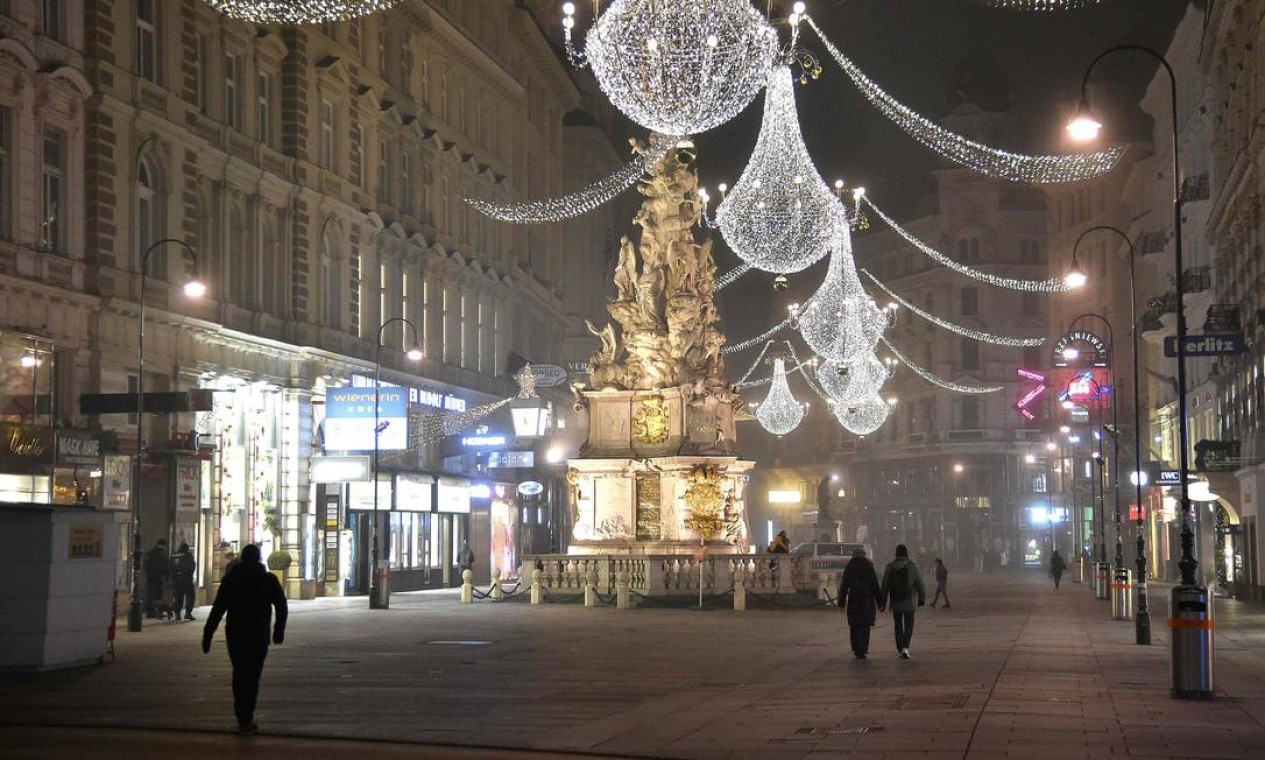 Pessoas caminham no centro da cidade quase deserta de Viena na véspera de Ano Novo, durante a nova pandemia de coronavírus. A Áustria entrou em seu terceiro bloqueio por coronavírus em 26 de dezembro até 24 de janeiro de 2021, enquanto o país batalha para reduzir sua taxa de infecção Foto: HANS PUNZ / AFP