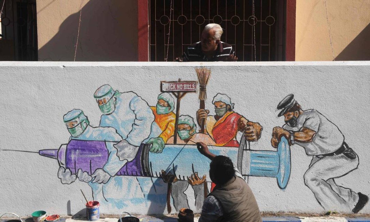 Artista dá os retoques finais em um mural que retrata trabalhadores da linha de frente carregando uma vacina contra a Covid-19, em Calcutá, na Índia Foto: DIBYANGSHU SARKAR / AFP