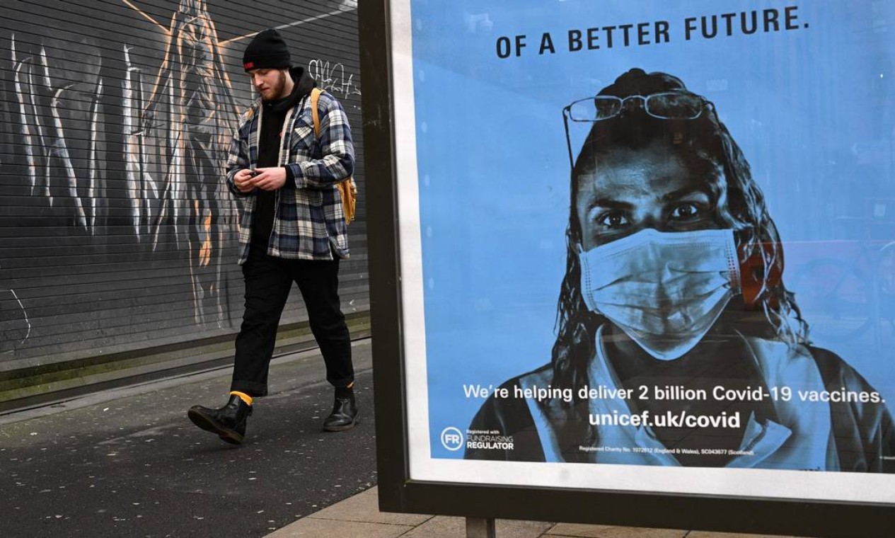Pedestre passa por um pôster da Unicef, promovendo as vacinas da Covid-19, em Manchester Foto: OLI SCARFF / AFP