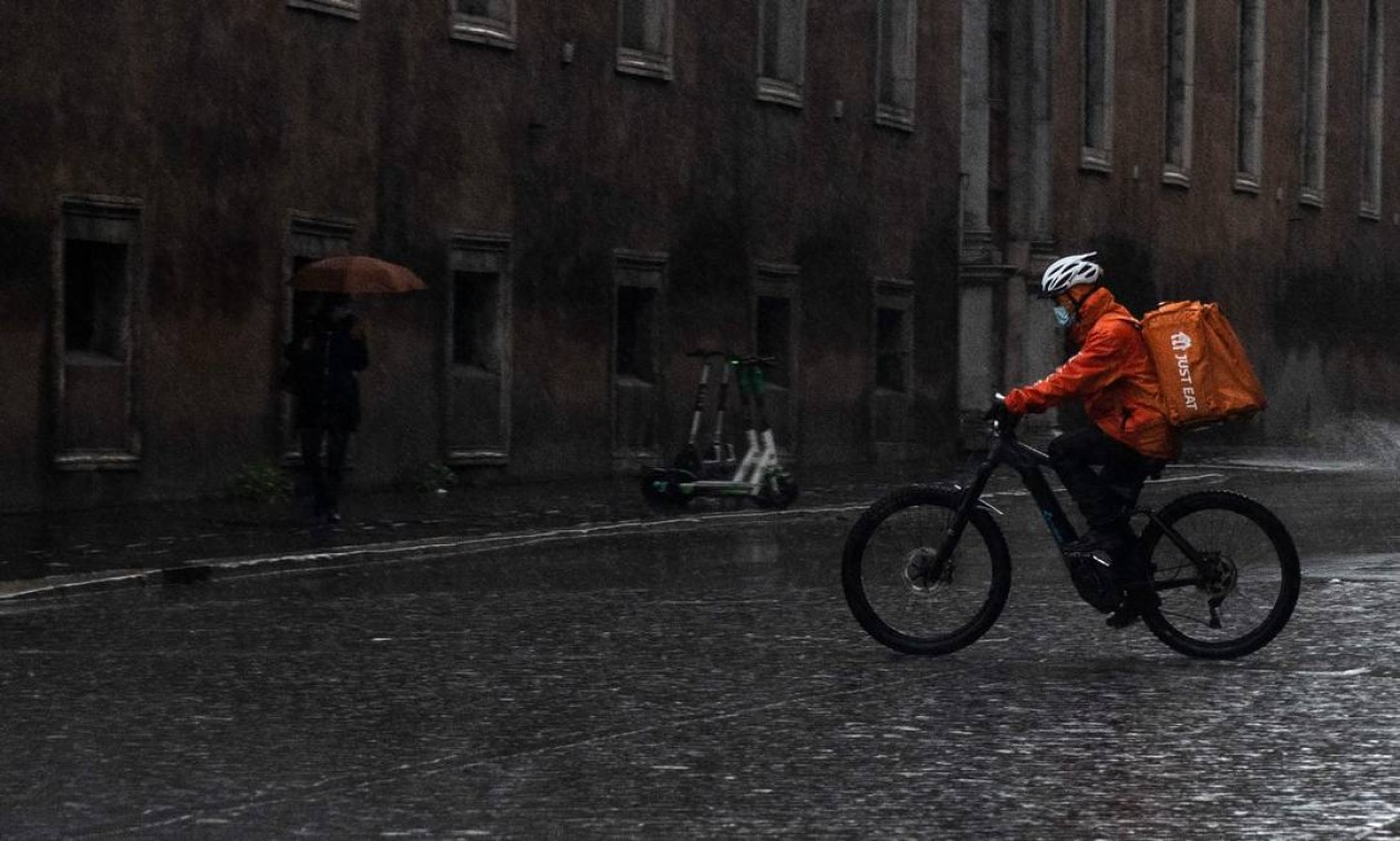 Um ciclista de entrega de comida pedala na chuva no centro de Roma. Itália também tomou decisões semelhantes um dia após Inglaterra e Escócia anunciarem o retorno a uma quarentena total Foto: TIZIANA FABI / AFP