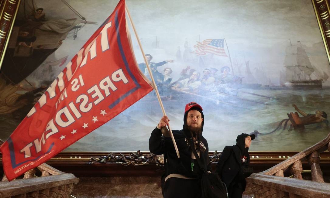 Um manifestante segura uma bandeira de apoio ao presidente Trump dentro do edifício do Capitólio dos EUA, perto do Senado. Foto: WIN MCNAMEE / AFP