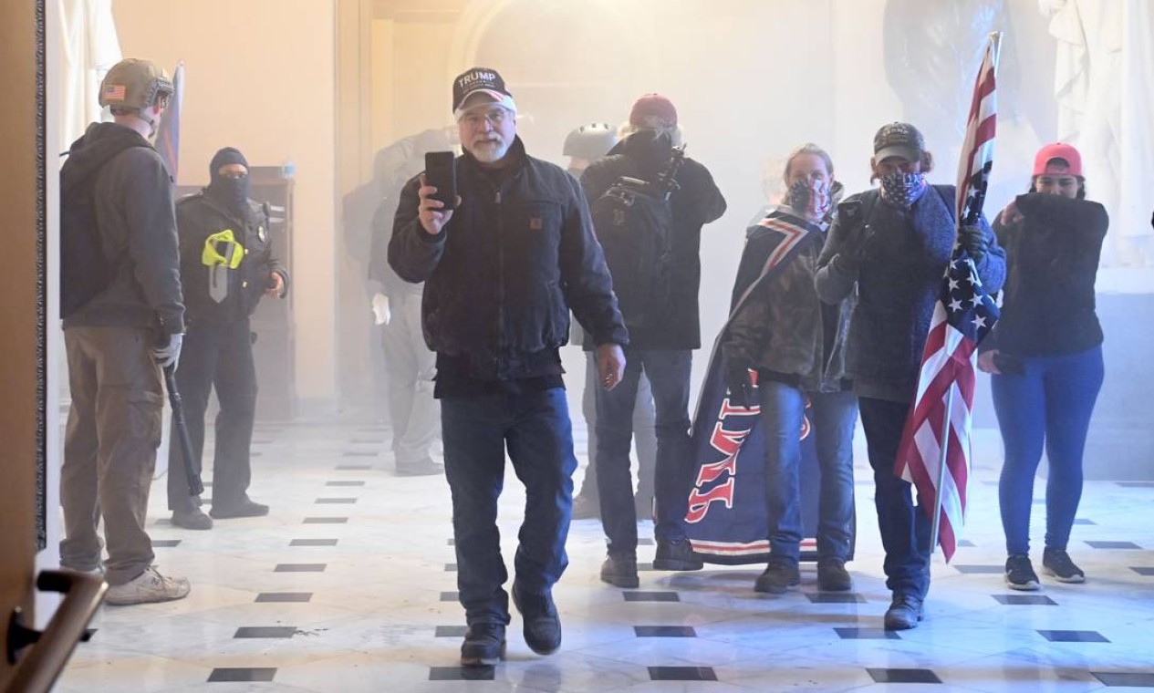 Apoiadores do presidente Donald Trump entram no Capitólio enquanto gás lacrimogêneo lançado pela polícia toma o corredor do prédio Foto: SAUL LOEB / AFP