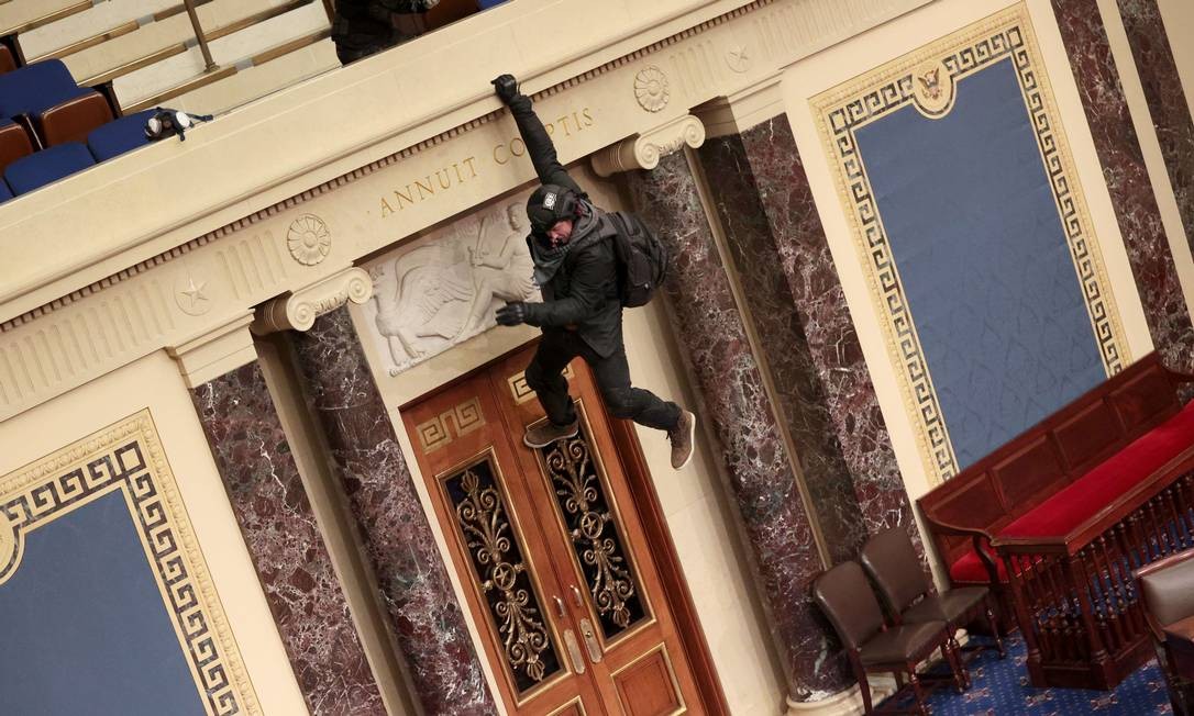 Um manifestante é visto pendurado na varanda do pelnário do Senado Foto: WIN MCNAMEE / AFP