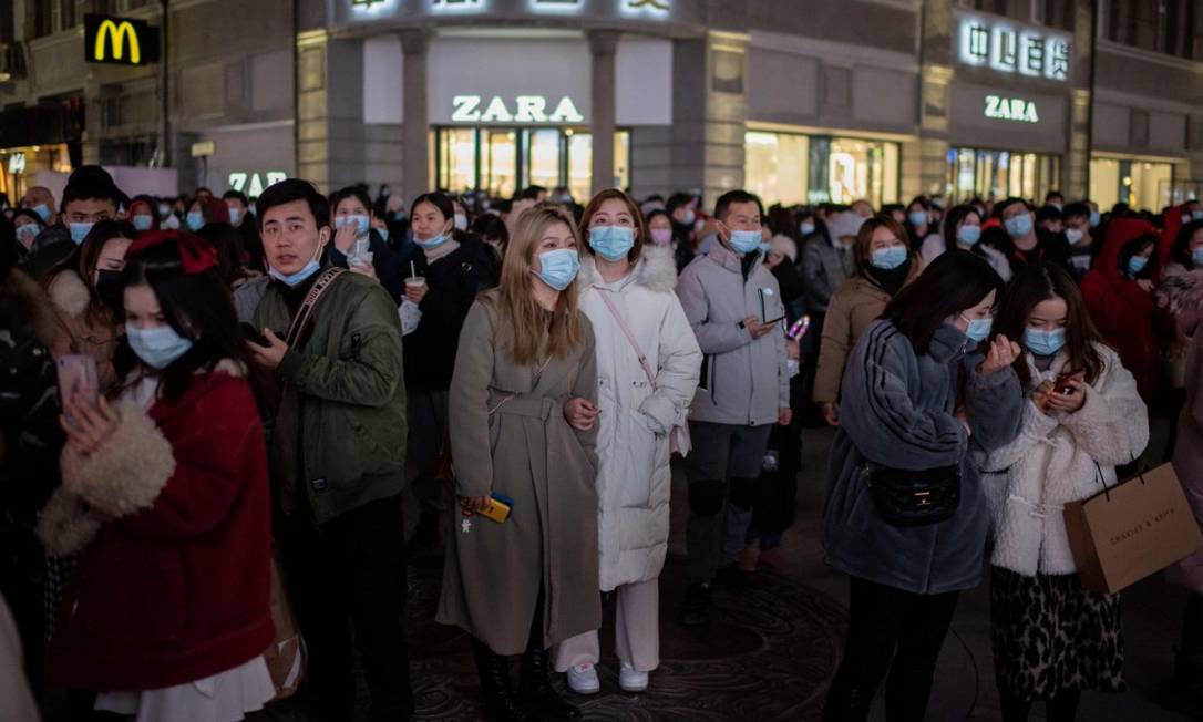 Pessoas usando máscaras em volta de uma tela 3D gigante na Rua Jianghan, em Wuhan, na véspera de completar um ano a primeira morte confirmada por coronavírus na China Foto: NICOLAS ASFOURI / AFP