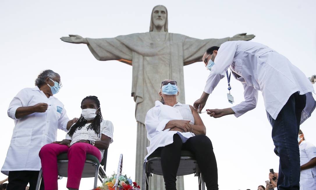 Dulcineia da Silva Lopes, 59 anos, recebe vacina Coronavac diante da estátua do Cristo Redentor, no Rio de Janeiro. Ao lado dela, à esquerda, Therezinha da Conceição, 80, foram as primeiras moradoras do Rio a receberem a vacina em Foto: Ricardo Moares / Reuters - 18/01/2020