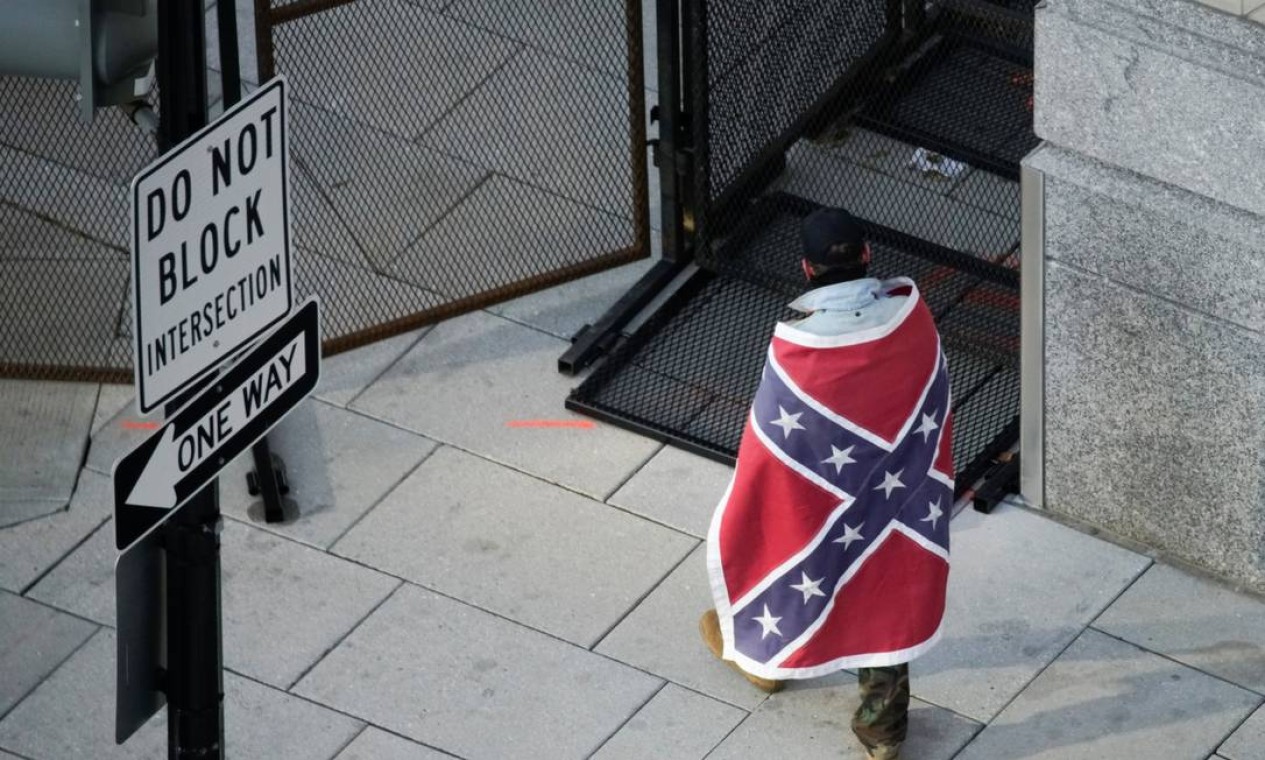 Homem envolto em uma bandeira confederada, um símbolo de ódio racial, caminha próximo ao perímetro de segurança do Capitólio dos EUA, em Washington Foto: EDUARDO MUNOZ / REUTERS