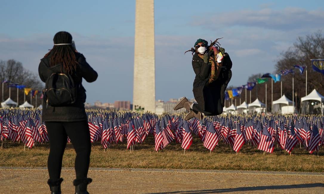 Mulher pula para uma foto em frente ao &#034;Campo de bandeiras&#034; e ao Monumento a Washington Foto: ALLISON SHELLEY / REUTERS