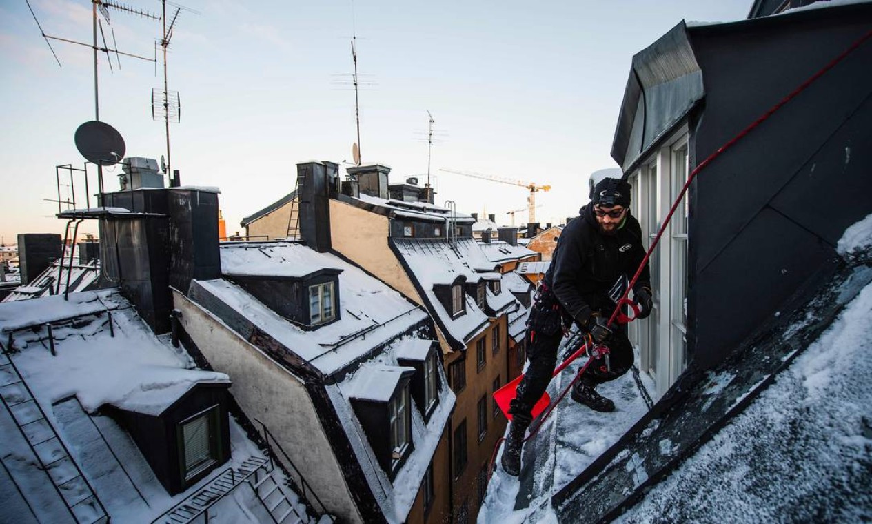 O removedor de neve de telhado Andrei Plian trabalha no topo de um dos edifícios da cidade velha de Stockholms, em Estocolmo Foto: JONATHAN NACKSTRAND / AFP - 11/02/2021