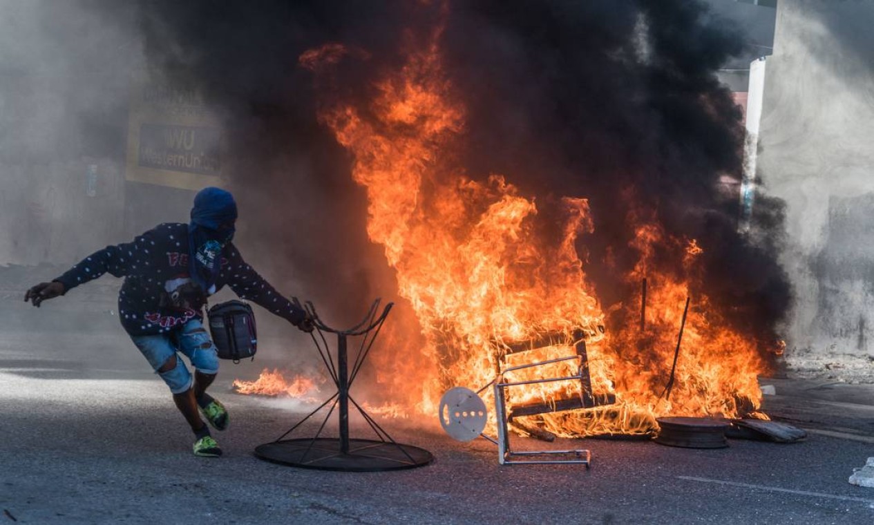 Manifestante alimenta fogueira durante protesto contra uma nova ditadura e o apoio internacional ao presidente Jovenel Moise, na capital Porto Príncipe Foto: REGINALD LOUISSAINT JR / AFP