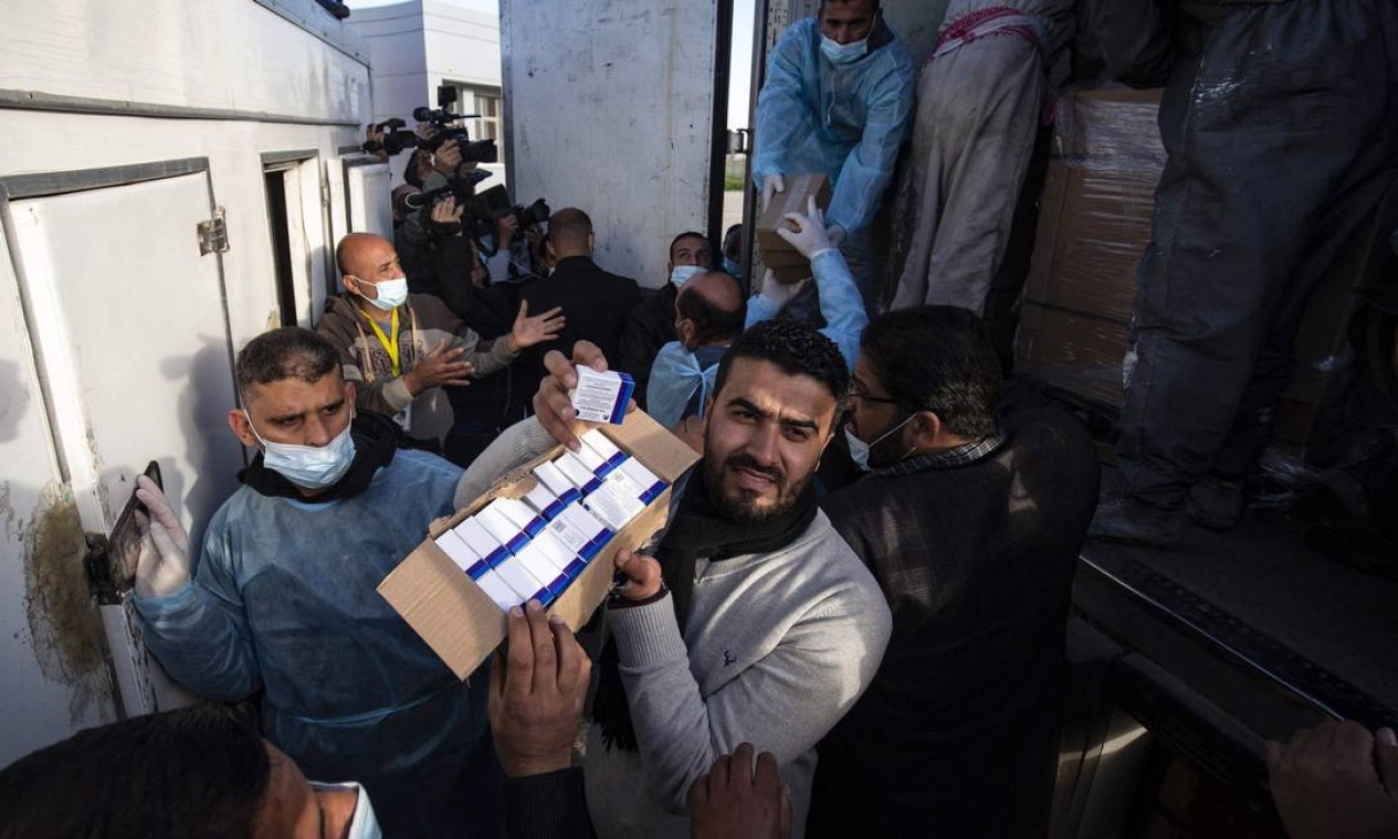 Trabalhadores descarregam caminhão comdoses da vacina russa Sputnik V, enviada dos Emirados Árabes Unidos, para a Faixa de Gaza através da travessia de Rafah com o Egito. Cerca de 20.000 doses da vacina contra o coronavírus dos Emirados Árabes Unidos chegou a Gaza hoje, uma entrega supostamente orquestrada por um rival do presidente palestino Mahmud Abbas três meses antes das eleições palestinas marcadas Foto: SAID KHATIB / AFP