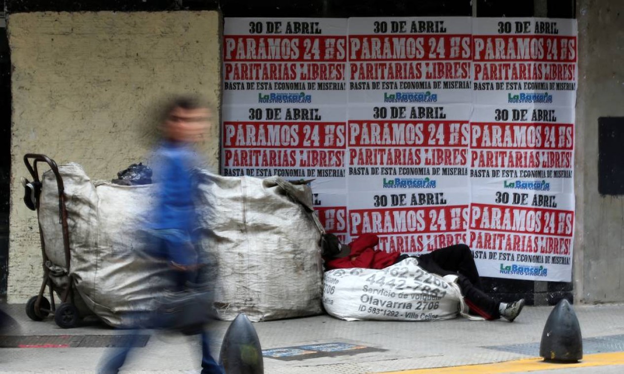 Morador de rua dorme do lado de fora de uma casa de câmbio com cartazes anunciando uma greve geral, em abril de 2019; país experimenta, desde 2018, um coquetel de disparada do dólar, dos juros, da inflação e do desemprego Foto: Agustin Marcarian / Reuters