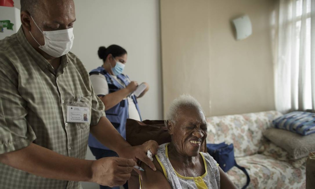 O técnico de enfermagem Milton Gomes Nunes Júnior aplica a vacina em Maria Palmira Maximiliano, de 87 anos, enquanto a agente comunitária Íris da Silva Brito preenche as carteirinhas de vacinação Foto: Márcia Foletto / Agência O Globo