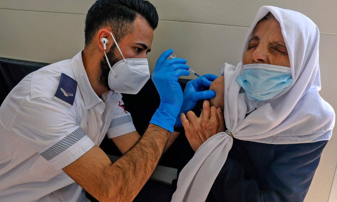 Paramédico aplica vacina em mulher palestina na Cidade Velha de Jerusalém Foto: AHMAD GHARABLI / AFP